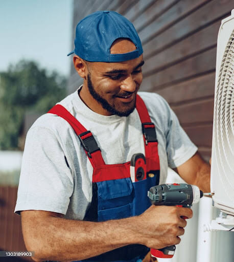 HVAC technician using a drill on an outdoor AC unit